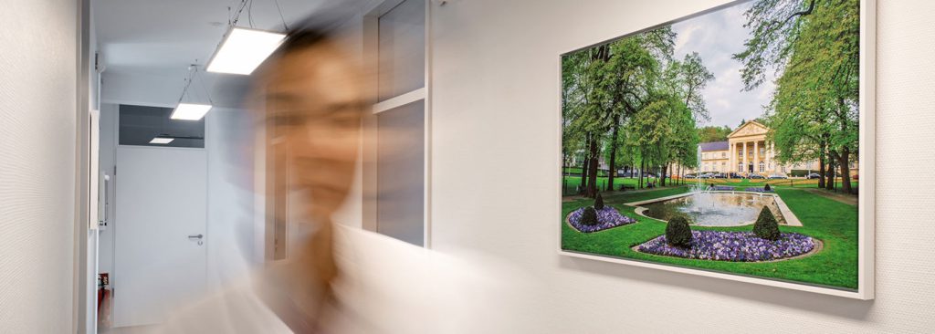 Unscharfe Person in Praxisflur mit dekorativer Fotografie des Quellenhof Aachen